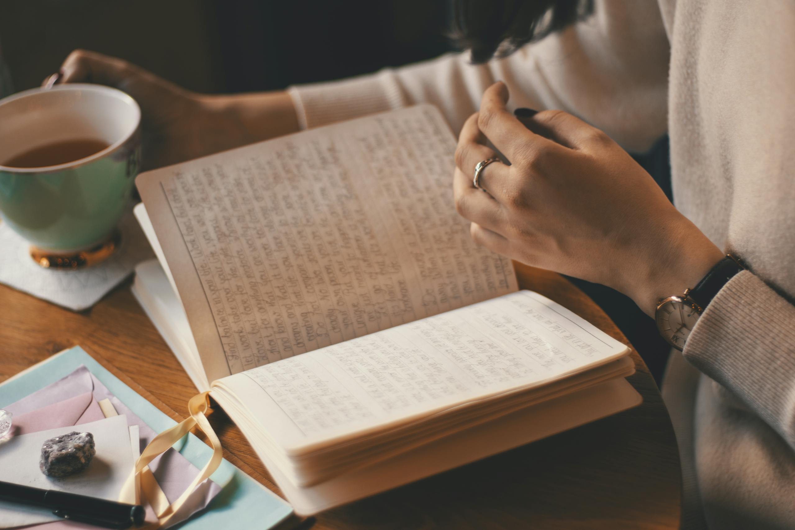 Home 6 A woman writes in a journal while enjoying a cup of coffee at a wooden table.